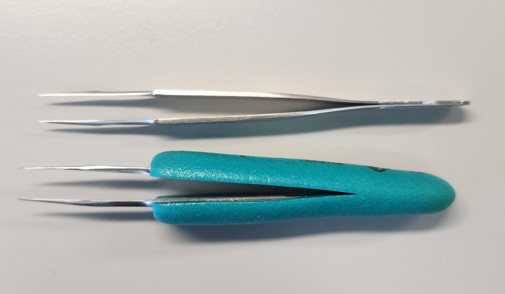 2 silver foreceps on a grey background. The bottom forecep has teal padding around the handle to provide better traction/grip.