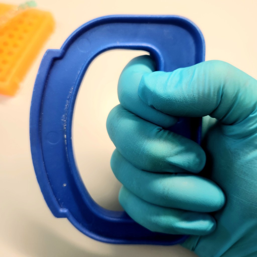 A teal gloved hand holds the bright blue Cap- It tool, providing a side view.